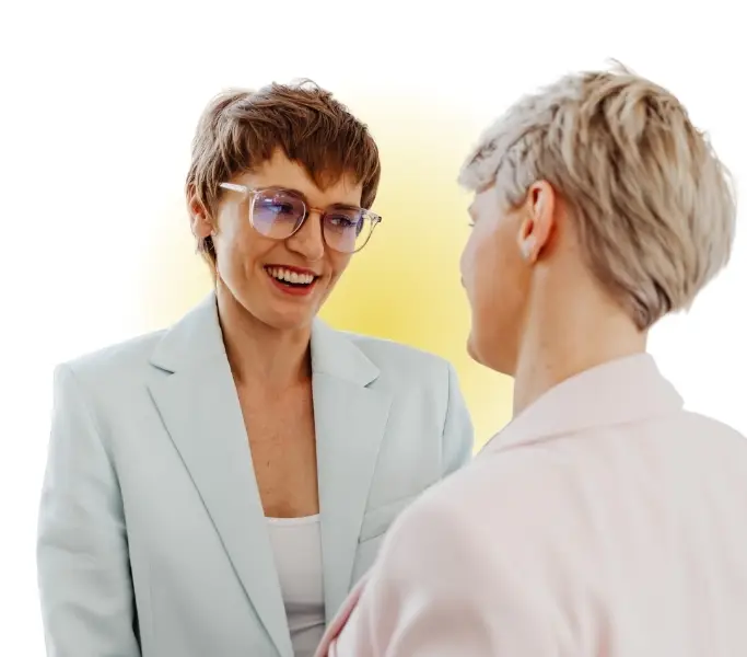 Das Bild zeigt zwei Frauen, die sich ansehen. Eine Frau sieht man direkt, die andere von hinten. Das Bild drückt Empathie im Gespräch aus.