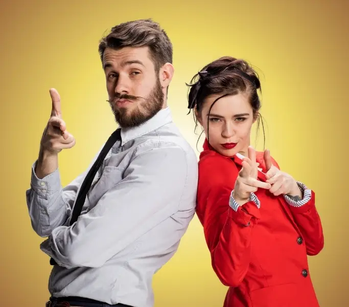 Mann und Frau vor gelbem Hintergrund, Schulter an Schulter, beide zeigen mit ihren Fingern in deine Richtung.