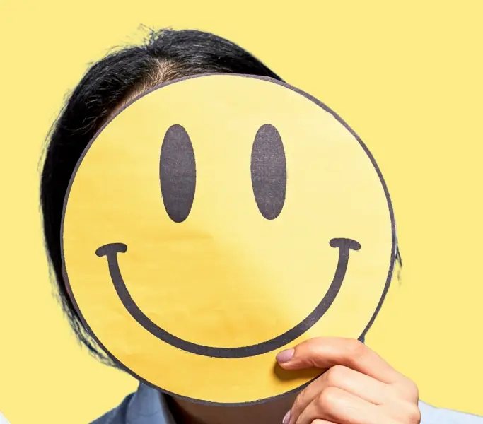 Gelber Hintergrund, darauf eine Frau mit Maske vor dem Gesicht, die ein Smiley ist