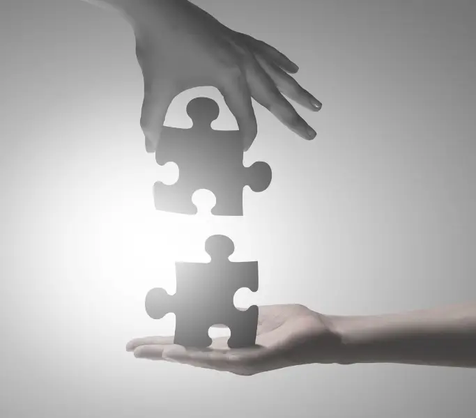 2 Hände, die übereinander abgebildet sind und jeweils 2 Puzzleteile in der Hand halten