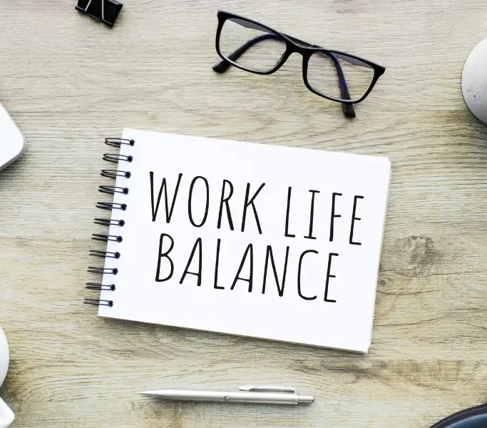 Work-Life-Balance Schild auf grauem Hintergrund und Brille mit schwarzem Rahmen rechts im Bild
