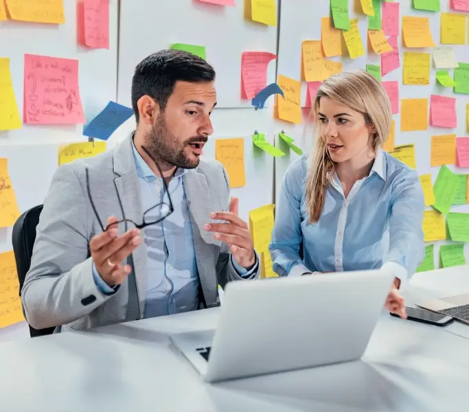 Überforderung gezeigt an einer Frau und einem Mann mit vielen bunten Post-its im Hintergrund